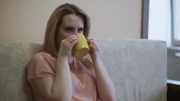 สาวสวยนั่งอยู่ที่บ้านในกักกัน หยิบรีโมท ดื่มชาร้อนๆ ดูทีวี สนุกกับการนั่งโซฟาในอพาร์ทเม้นท์ — วีดีโอสต็อก