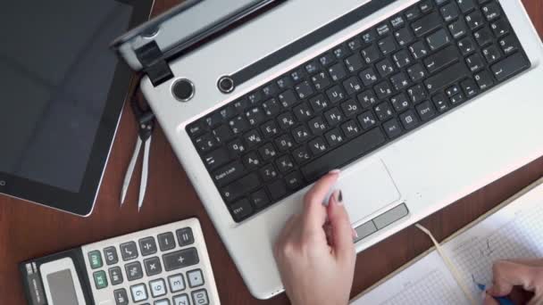 Um homem trabalha num computador. Vista de cima. Tipos em um teclado de computador portátil, escreve dados a um caderno. Trabalho remoto — Vídeo de Stock