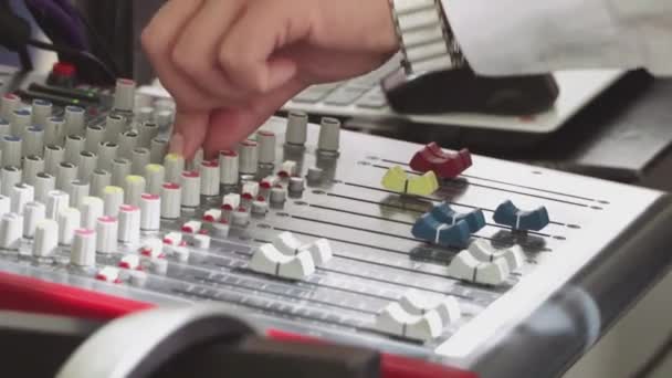 A DJ kezei megérintik az elektronikus zenét játszó gombokat és csúszkákat. Egy profi DJ úgy állítja be a keverőasztalon lévő vezérlőket és gombokat, hogy erőteljes hangot hozzon létre egy partin vagy stúdióban. — Stock videók