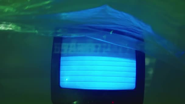Dans un studio avec un feu vert, le téléviseur joue statique, et une feuille transparente flotte autour. Mouvement abstrait d'un film transparent de haut en bas devant une télévision — Video