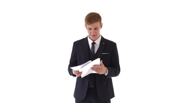 A young, handsome man in a jacket checks documents, payments, a report. Businessman isolated on a white background. He is pleased with the work of the corporate staff. He smiles and enjoys looking at — Stock Video