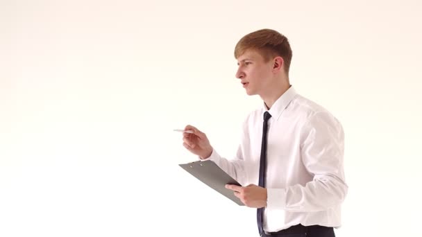 Atractivo hombre de negocios de pie en un traje blanco y corbata, sosteniendo una pluma estilográfica y documentos en su mano. Él llevará a cabo el cálculo, comparar los números en los documentos. Fondo blanco — Vídeos de Stock