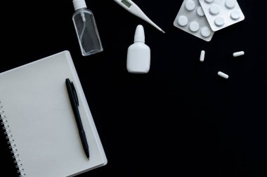 Siyah arkaplanda termometrenin, hapların ve defterin üst görünümü