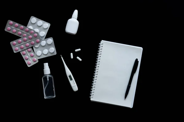 Siyah arkaplanda termometrenin, hapların ve defterin üst görünümü