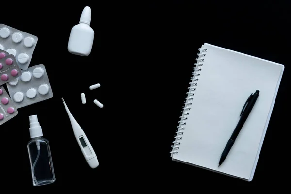 Siyah arkaplanda termometrenin, hapların ve defterin üst görünümü