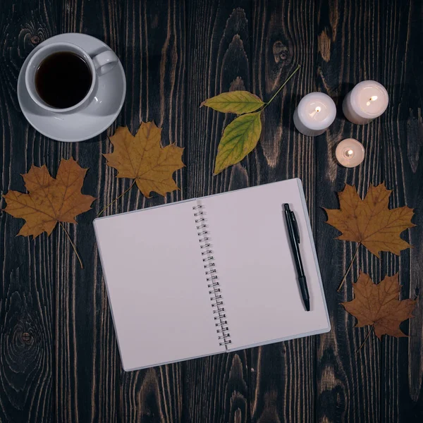 Boş not defterinin üst görüntüsü, bir fincan kahve ve ahşap arka planda düşen yapraklar.