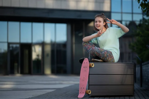 Şık bir genç sokakta kaykay üstüne peni tahtasıyla oturup dinlenir.