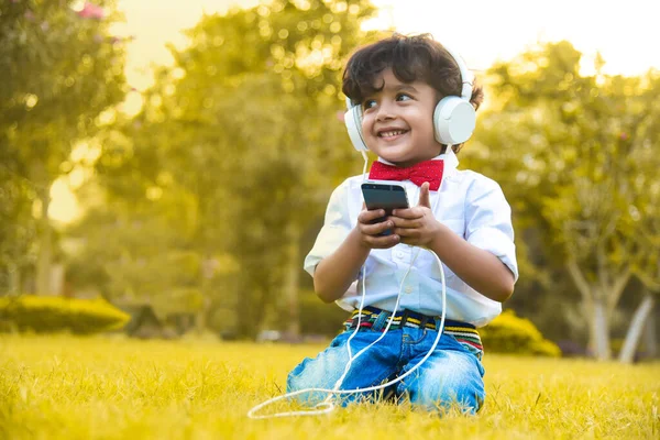 Mały Chłopiec Słuchający Muzyki Telefonu Swoich Białych Słuchawkach Parku — Zdjęcie stockowe