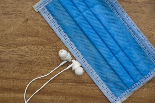 Tıbbi mavi yüz maskesi ve ahşap arka planda beyaz kulaklık. Müzisyen konsepti için güvenlik.