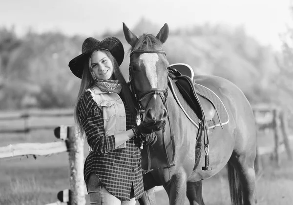 cowgirl in a hat standing near a horse in a field