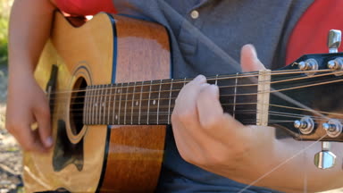 Bir adam gitar yaz aylarında göl kıyısında oynuyor.