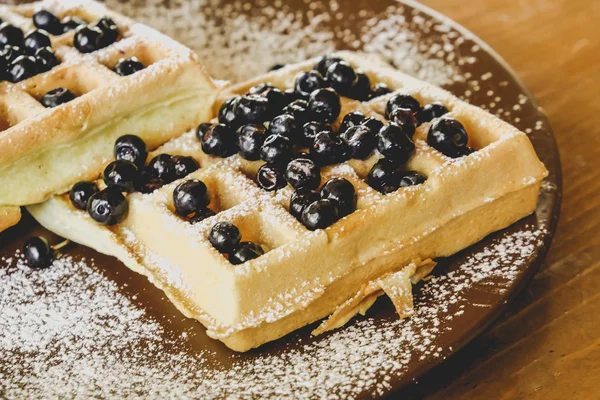 Belgian waffles with berries on a plate with powdered sugar.