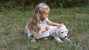 küçük kız çimlerin üzerine yaz aylarında bir golden retriever köpek yavrusu ile oynuyor.