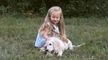küçük kız çimlerin üzerine yaz aylarında bir golden retriever köpek yavrusu ile oynuyor.
