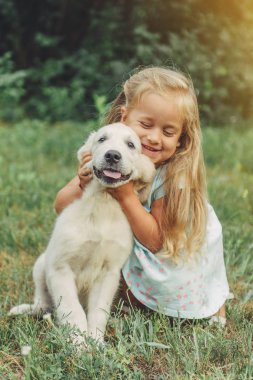 Küçük şirin sarışın kız onu köpek yavrusu golden retriever ile yaz aylarında parkta oynarken..