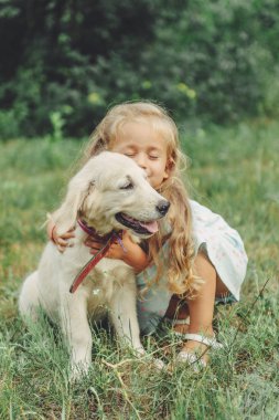 Küçük şirin sarışın kız onu köpek yavrusu golden retriever ile yaz aylarında parkta oynarken..