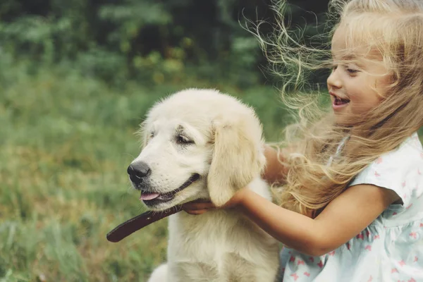 Küçük şirin sarışın kız onu köpek yavrusu golden retriever ile yaz aylarında parkta oynarken..