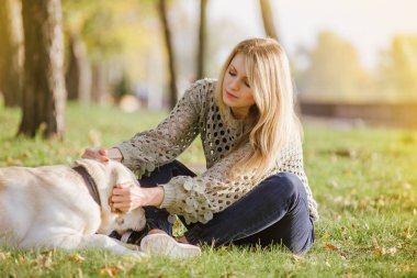 güzel sarışın parkta çim üzerinde oturan ve onu köpek labrador ile oynamak