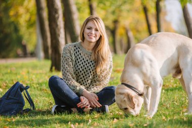 güzel sarışın parkta çim üzerinde oturan ve onu köpek labrador ile oynamak