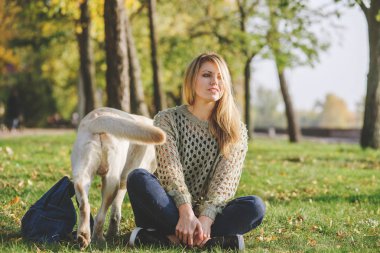 güzel sarışın parkta çim üzerinde oturan ve onu köpek labrador ile oynamak