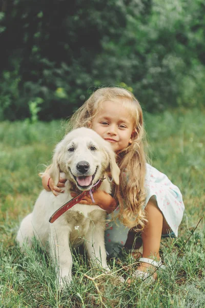 Petite fille blonde mignonne jouant avec son chiot golden retriever . — Photo