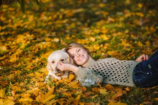 Une belle blonde gît dans des feuilles jaunes dans un parc et joue avec son labrador . — Photo