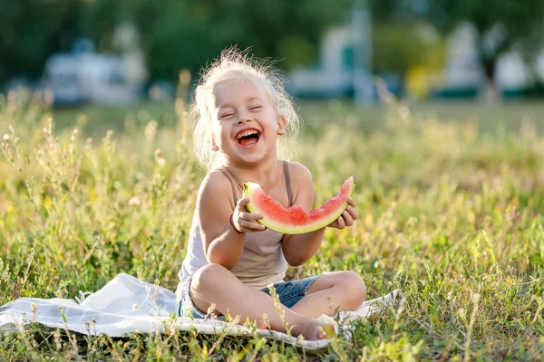 Küçük sarışın kız yaz parkında karpuz yiyor..