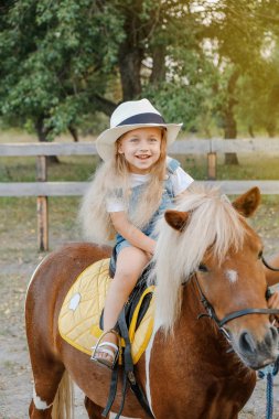 Sevimli küçük sarışın kız sonbaharda bir midilli üzerinde oturuyor.