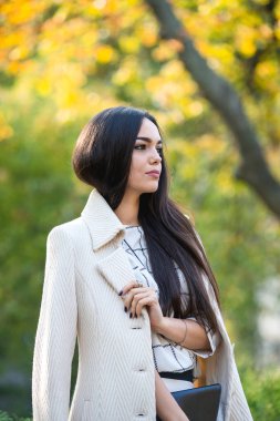 Genç güzel iş kadını sonbaharda parkta duruyor.