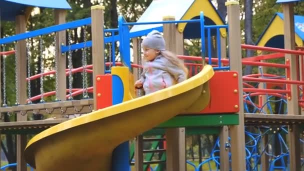 Uma menina brinca no playground e monta um slide na queda no parque . — Vídeo de Stock