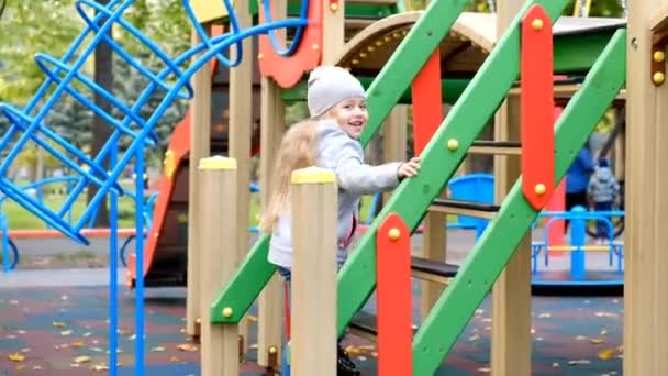 Een klein meisje speelt op de speelplaats en rijdt een dia in de herfst in het park. — Stockvideo