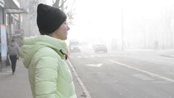 Uma jovem mulher está de pé em uma rua da cidade em névoa grossa . — Vídeo de Stock