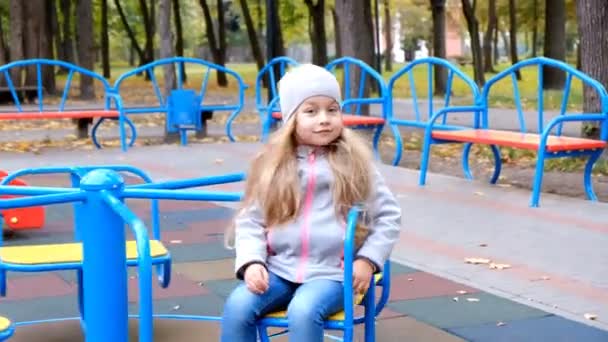 Маленькая девочка едет на качелях на детской площадке в парке осенью . — стоковое видео