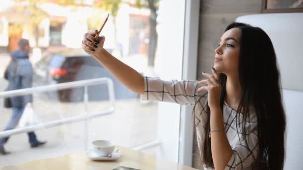 Jovem bela morena leva uma selfie em um café . — Vídeo de Stock