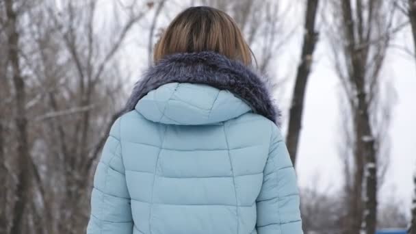 Молодая женщина зимой ходит по заснеженной дороге в парке — стоковое видео