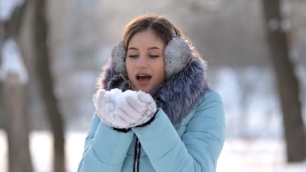 Hermosa joven mujer sosteniendo la nieve en sus manos y soplando en ella — Vídeos de Stock