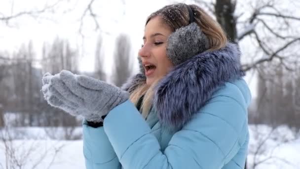 Красивая молодая женщина держит снег в руках и дует на него — стоковое видео