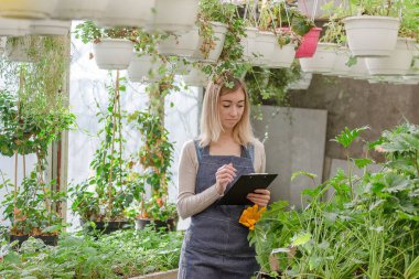 Genç bir kadın bahçıvan bir serada çiçeklerin kaydını tutar..
