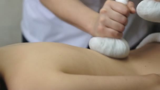 Профессиональный массажист делает массаж спины молодой женщине с травяными сумками . — стоковое видео