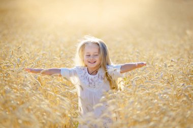 Küçük sarışın bir kız olgunlaşmış buğday tarlasında koşar ve gülümser..