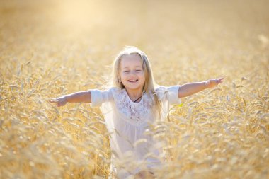 Küçük sarışın bir kız olgunlaşmış buğday tarlasında koşar ve gülümser..