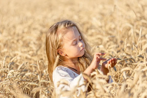 Niña rubia se para en un campo de trigo en verano y sonríe —  Fotos de Stock