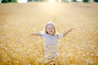 Küçük sarışın bir kız olgunlaşmış buğday tarlasında koşar ve gülümser..