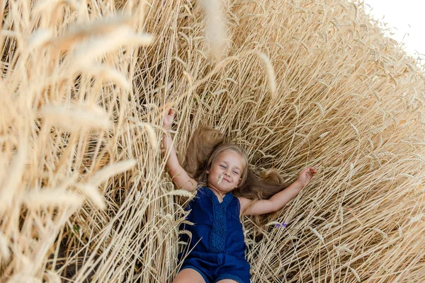 Malá dívka blondýny leží v pšeničném poli v létě — Stock fotografie