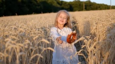 Küçük kız eğleniyor ve yazın buğday tarlasında çörek yiyor..