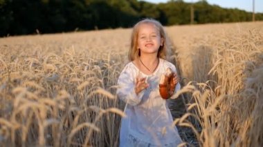 Küçük kız eğleniyor ve yazın buğday tarlasında çörek yiyor..