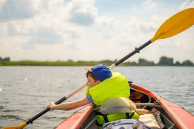 Küçük bir çocuk yazın nehirde kano yapar ve kürek çeker. Çocuk nehirde bir teknede yüzüyor..