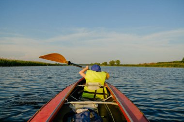 Küçük bir çocuk yazın nehirde kano yapar ve kürek çeker. Çocuk nehirde bir teknede yüzüyor..
