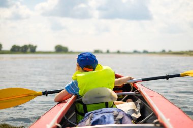 Küçük bir çocuk yazın nehirde kano yapar ve kürek çeker. Çocuk nehirde bir teknede yüzüyor..