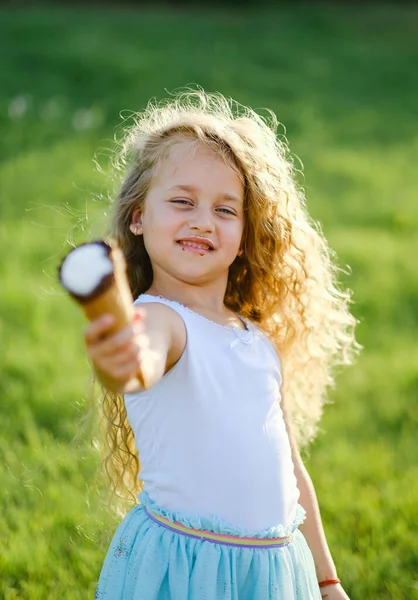 Little blonde girl with long hair has fun eating ice cream in a summer park. A girl walks in the summer park and eats ice cream. Happy childhood and happy summer.